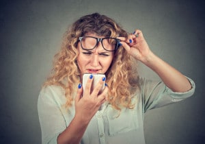 woman with glasses having trouble seeing phone has vision problems