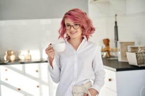 Smiling young teen girl wearing white shirt and glasses drink tea in kitchen.