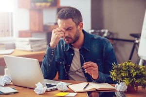 Feeling sick and tired. Frustrated young man massaging his nose and keeping eyes closed while sitting at his working place in office