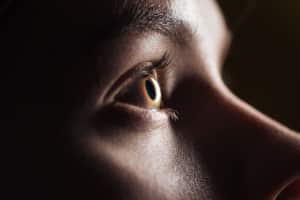 close up view of young woman eye with eyelashes and eyebrow looking away in darkness