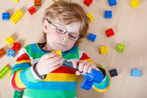 Little blond kid boy playing with lots of colorful plastic block